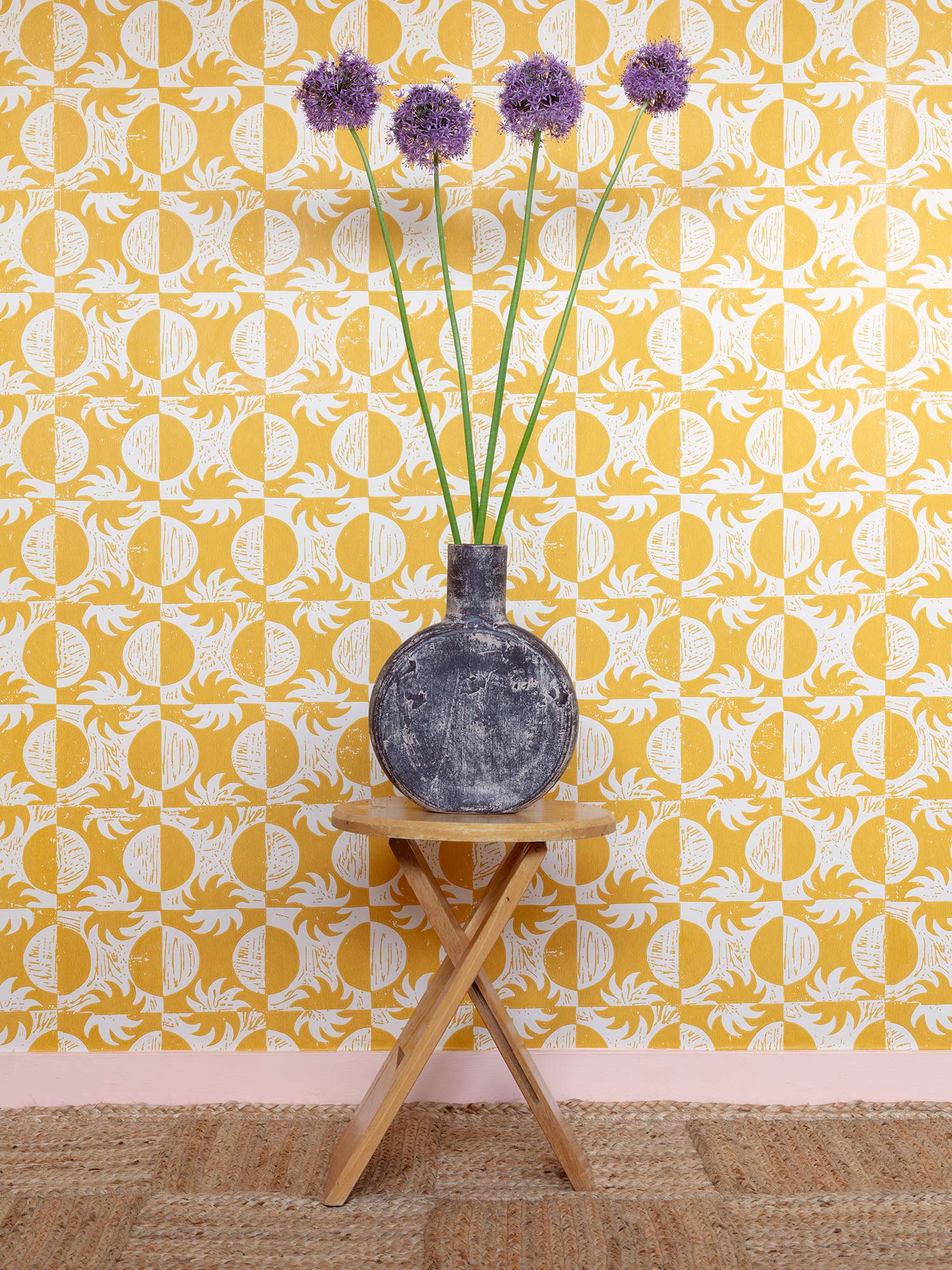 Yellow and off-white sun and moon surface printed wallpaper by contemporary artist Zoe Gibson with purple flowers in black ceramic vase