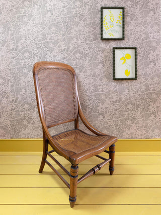 A pale pink wallpaper with cut-out black dashed bramble design, pictured with brown chair and yellow painted floorboards and artwork