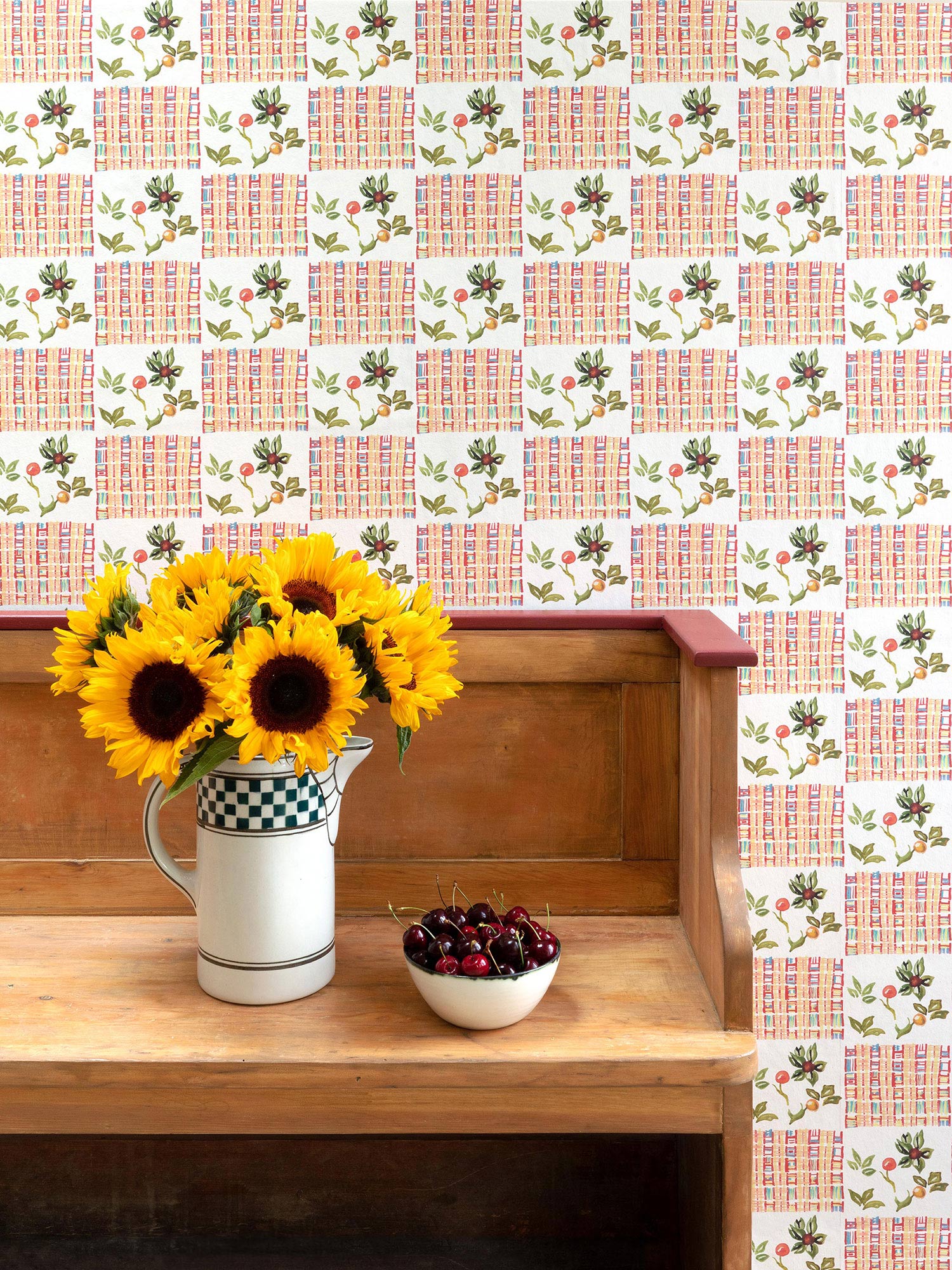 White chequerboard wallpaper combining Arts & Crafts with West African textiles, with a detail from a William Morris wall hanging, pictured with cherries and sunflowers on a bench