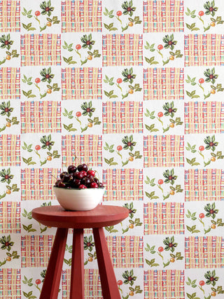 Maximalist white wallpaper combining Arts & Crafts with West African textiles, with a detail from a William Morris wall hanging, pictured with a bowl of cherries on a red stool