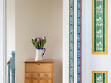 Striped green blue and yellow flowered wallpaper border from 1918 by Arts & Crafts artist CFA Voysey, pictured with flowers on chest of drawers