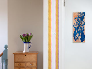 Striped yellow and pink wallpaper border from 1918 by Arts & Crafts artist CFA Voysey, pictured with flowers on chest of drawers