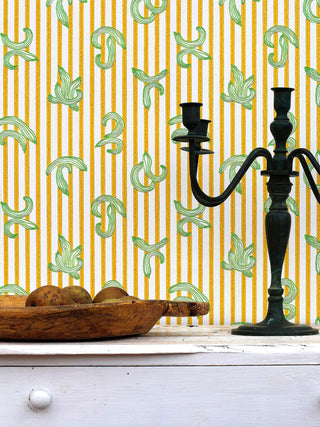 A quirky and eccentric wallpaper by artist Ferris featuring yellow stripes and green cucumber motifs, close-up with candle and fruit bowl