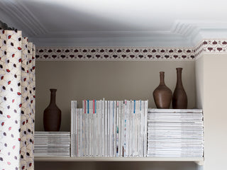 A wallpaper border depicting ivy leaves and wavy lines, originally hand-painted using wine-coloured ink, pictured here with vases and stacks of magazines