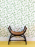 A green clover wallpaper on cream background, with flowing abundant stems and jaunty leaves, pictured with wooden stool and yellow painted floorboards