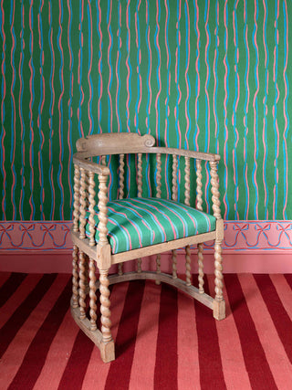 Wooden chair against green wallpaper backdrop featuring pink and blue vertical ribbon stripes and pink bow border