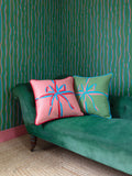 Pink and green square cushions with ribbons screenprint, sitting on green sofa with green striped wallpaper background