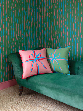 Pink and green square cushions with ribbons screenprint, sitting on green sofa with green striped wallpaper background