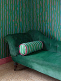 Hand-finished Regency Stripe-inspired bolster by artist Susie Green. Linen fabric with a high-quality feather inner, pink and blue stripes on green, pictured on green sofa