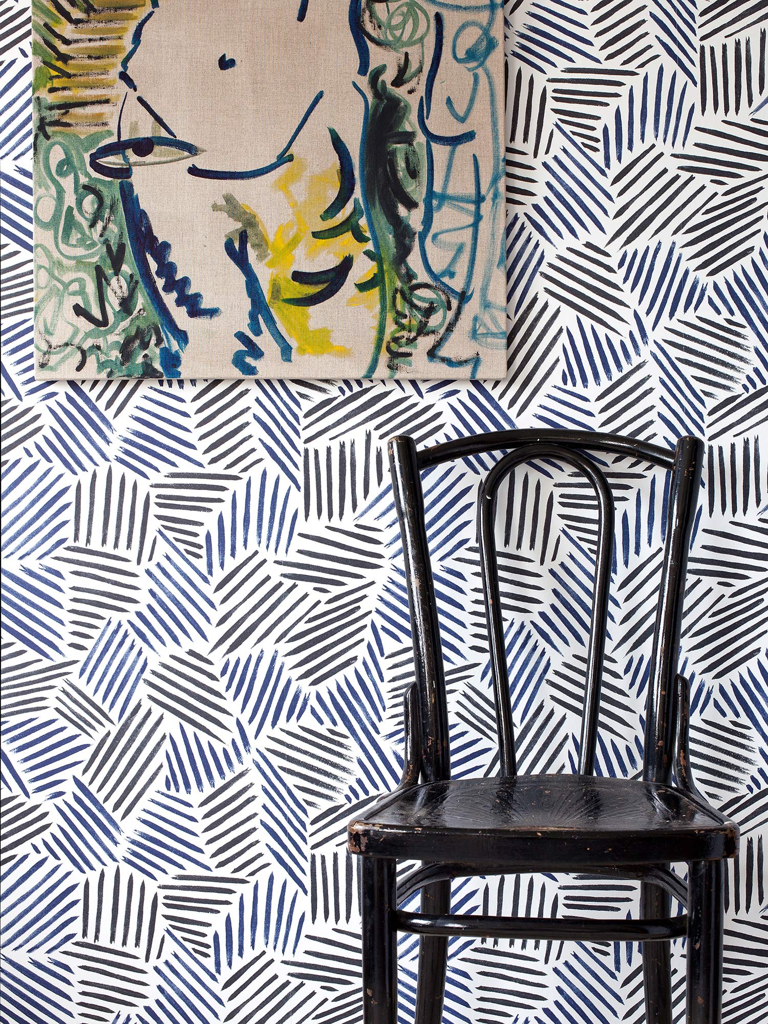 This wallpaper, inspired by New York artist Jasper Johns and the Bloomsbury Group, combines repeating black and navy blue brushstrokes to create a modern, abstract striped design, pictured with black chair and modern nude artwork