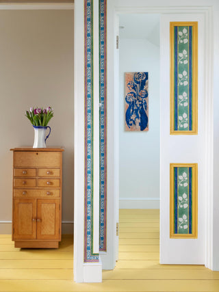 Striped green blue and yellow flowered wallpaper border from 1918 by Arts & Crafts artist CFA Voysey, pictured with flowers on chest of drawers and on white doorway