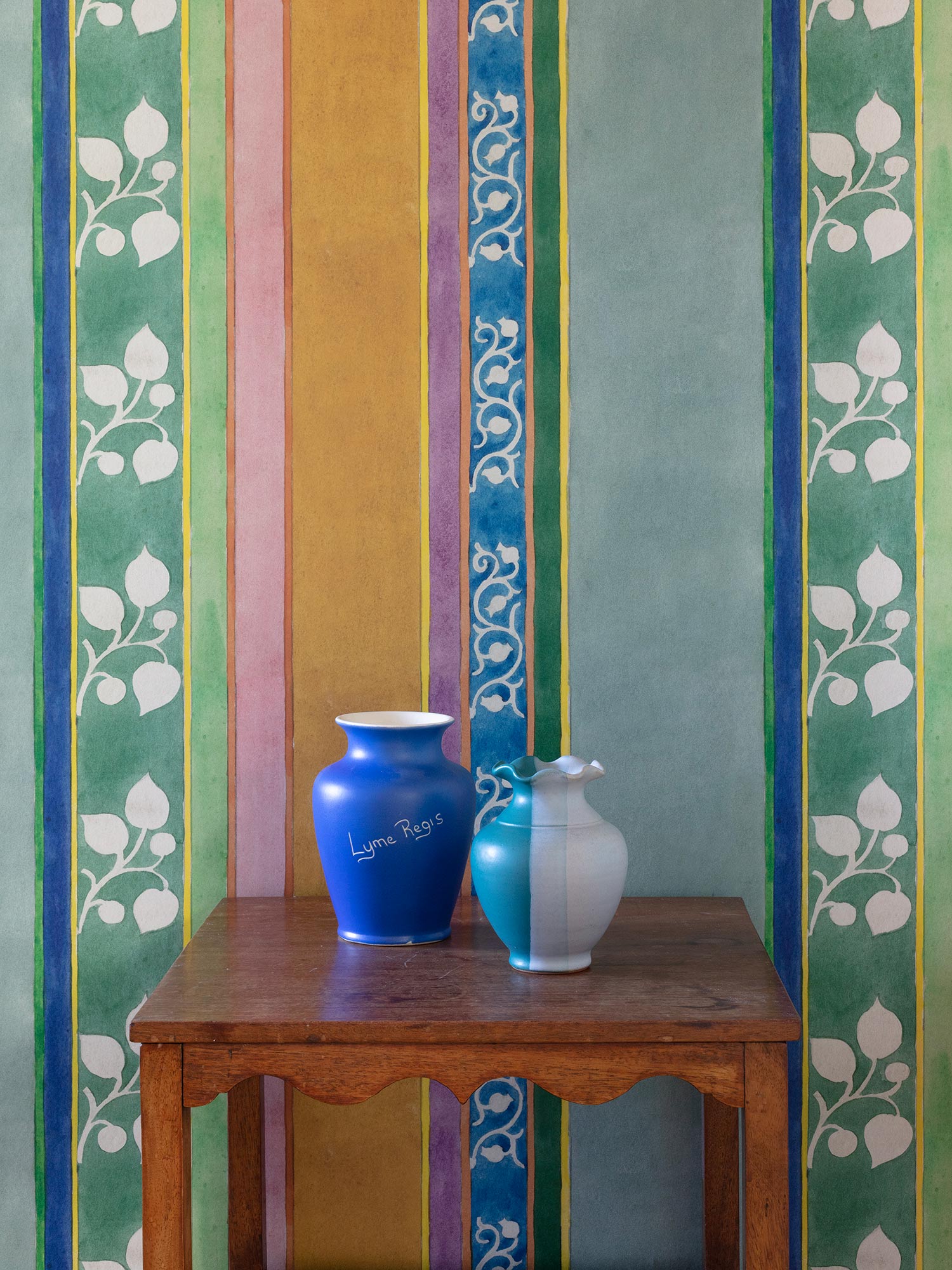 Striped green, pink, orange and blue wallpaper from 1918 by Arts & Crafts artist CFA Voysey, pictured with vases