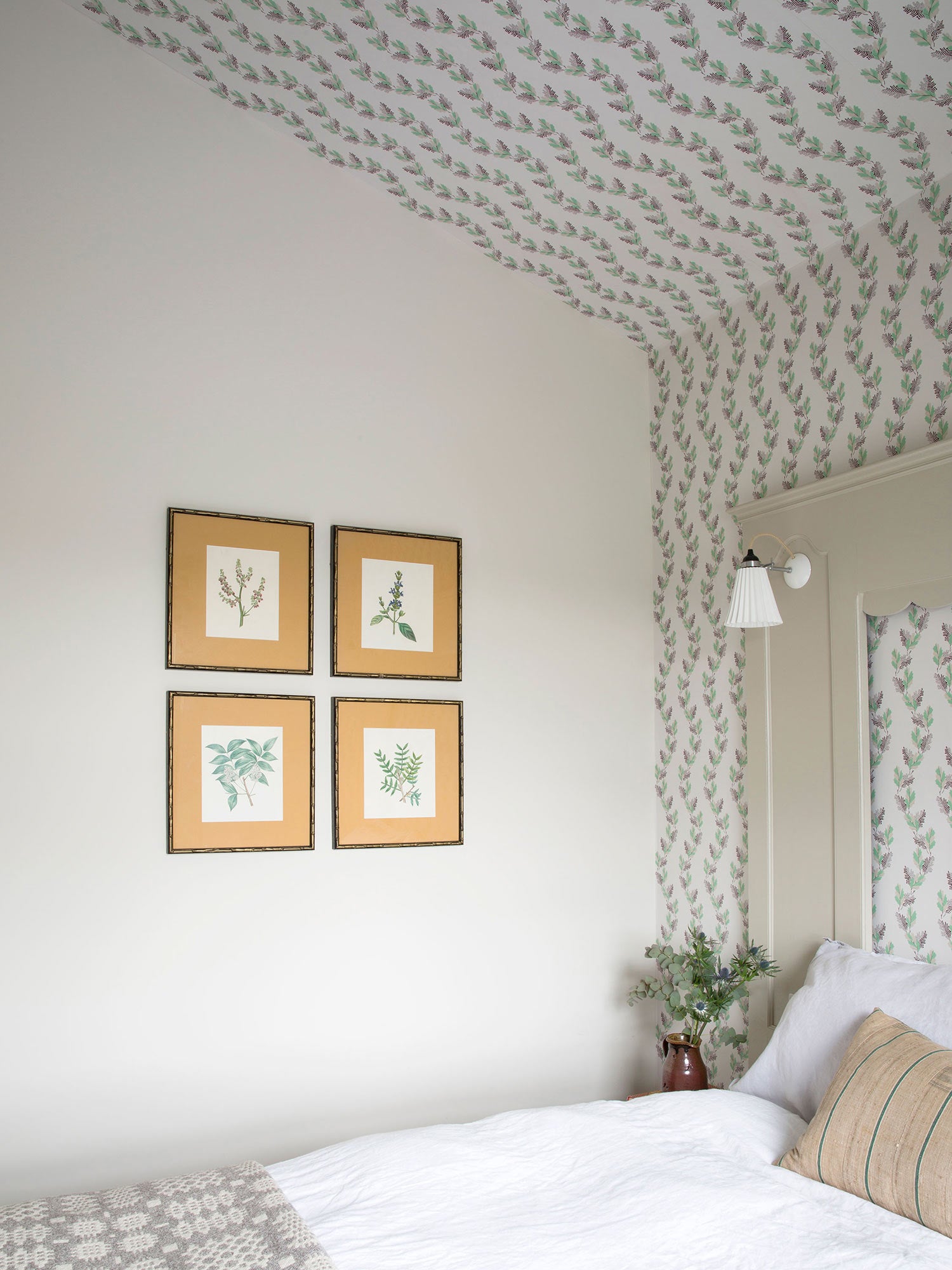 An archival design dating back to 1800, this wavy wallpaper displays falling oak leaves in green and brown, pictured as a wallpaper canopy over a bed